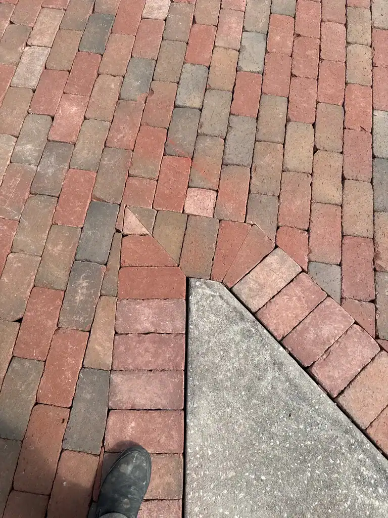 A brick sidewalk in Hernando County with a triangular concrete section intersecting it. The red and tan bricks include one at the corner set at an odd angle. Part of a shoe appears at the bottom left.
