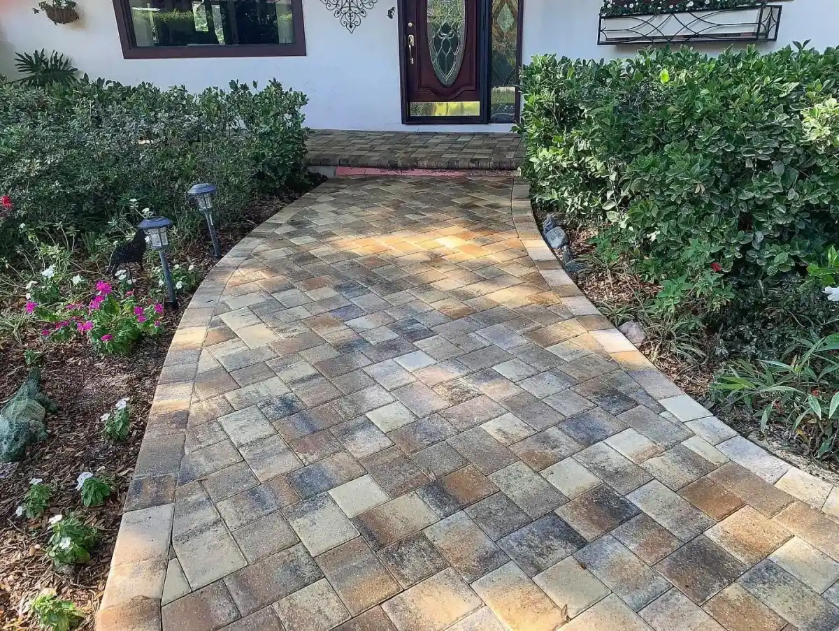 A curved walkway made of tan, brown, and gray pavers leads to a house entrance surrounded by green shrubs, flowering plants, and outdoor solar lights—crafted by an expert landscaper serving Citrus, FL, and Sumter.