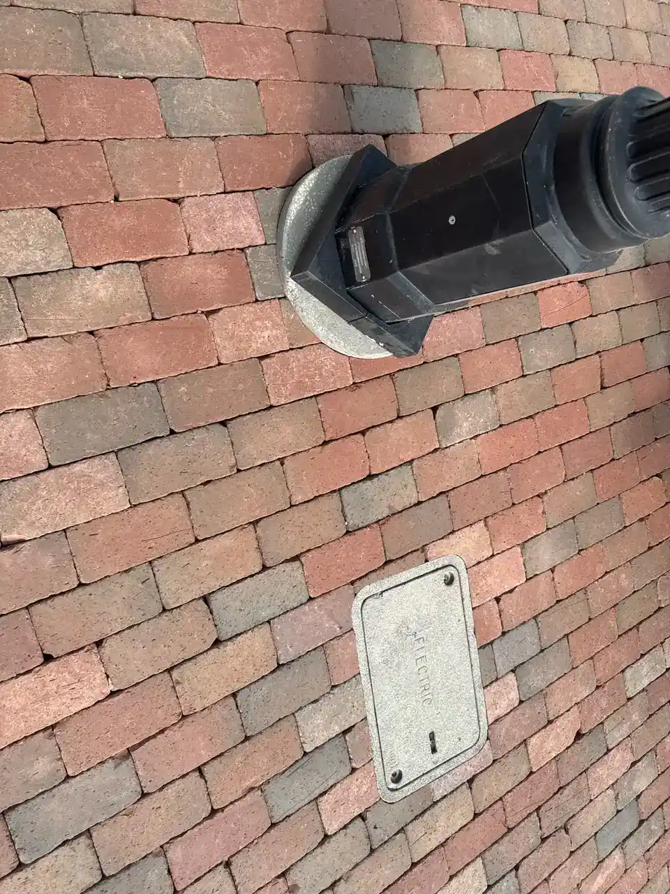 A black lamp post stands on a sidewalk made of reddish-brown bricks in Hernando County. Near the lamp post, a rectangular metal cover labeled “ELECTRIC” is embedded in the bricks.