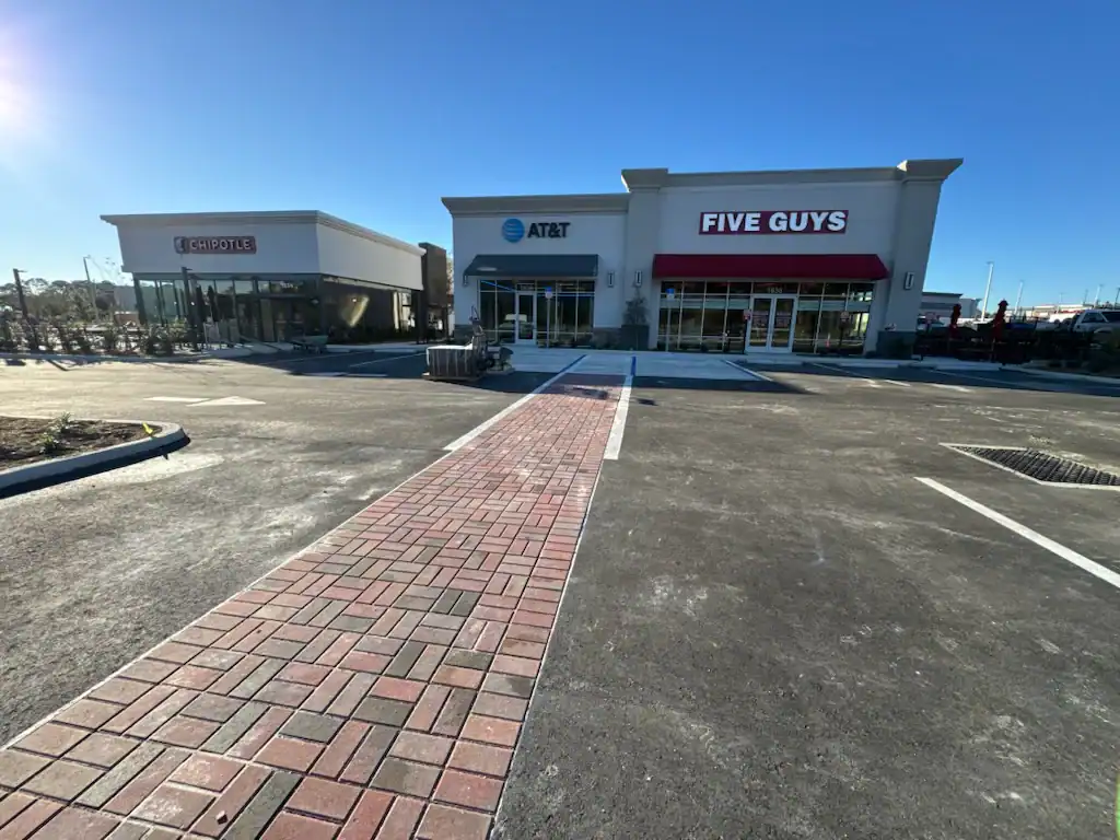 A brick walkway leads to storefronts for Chipotle, AT&T, and Five Guys in a shopping plaza on a clear, sunny day in Sumter, FL. The parking lot in front is mostly empty.