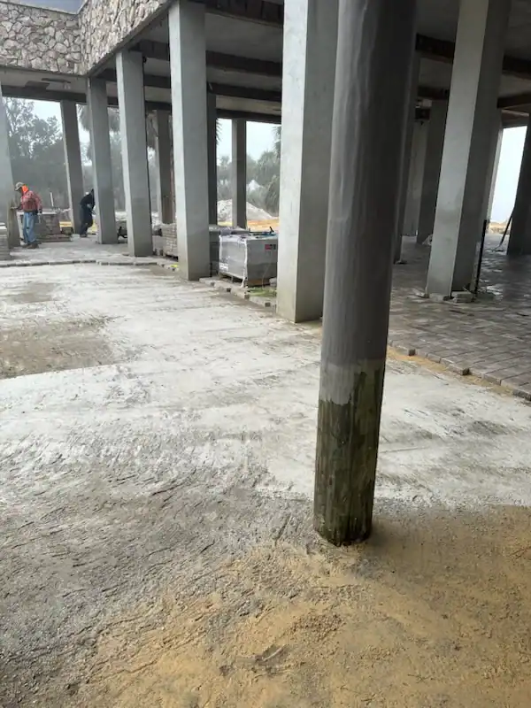 A wooden utility pole stands awkwardly in the middle of a paved walkway near a building under construction, where workers, building materials, and a landscaper from Citrus or Sumter, FL can be seen in the background.