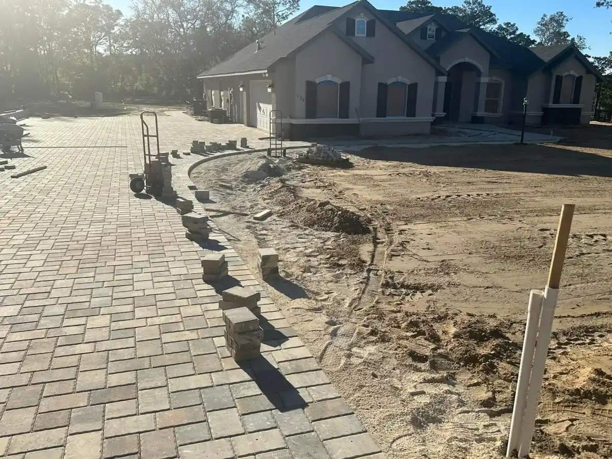 A partially completed brick driveway leads to a house in Hernando County, FL; pavers, tools, and sand are visible, highlighting ongoing construction and landscaping work by a skilled Landscaper Citrus.