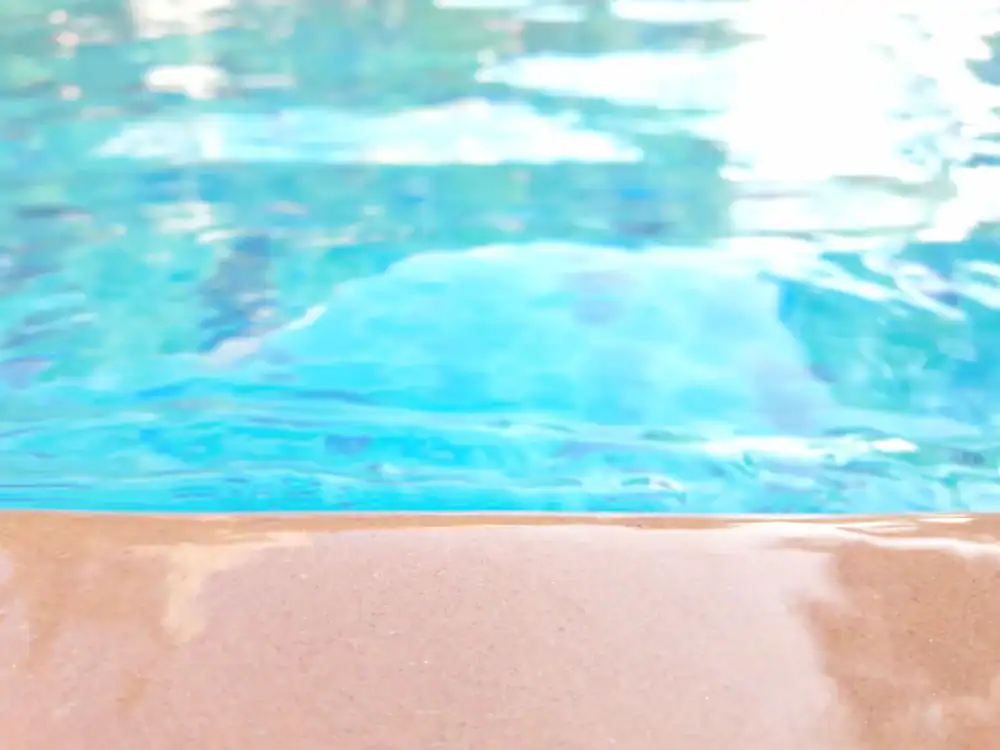 Close-up view of a swimming pool with clear blue water in Hernando County, FL, showing the edge of the pool in the foreground. The water appears calm and inviting, with reflections on the surface&mdash;perfect for a landscaper Citrus design.