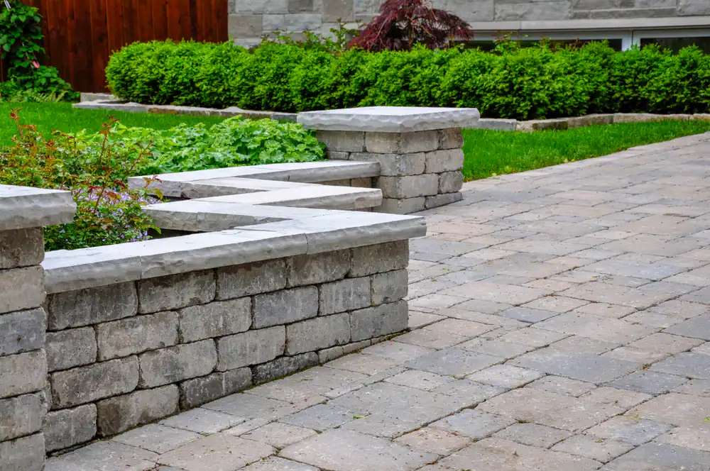 A landscaped yard in Hernando County, FL, with a stone patio, raised garden beds, and lush green shrubs. The pavers and stone walls offer a neat look&mdash;perfect inspiration from a skilled landscaper Citrus area residents trust.
