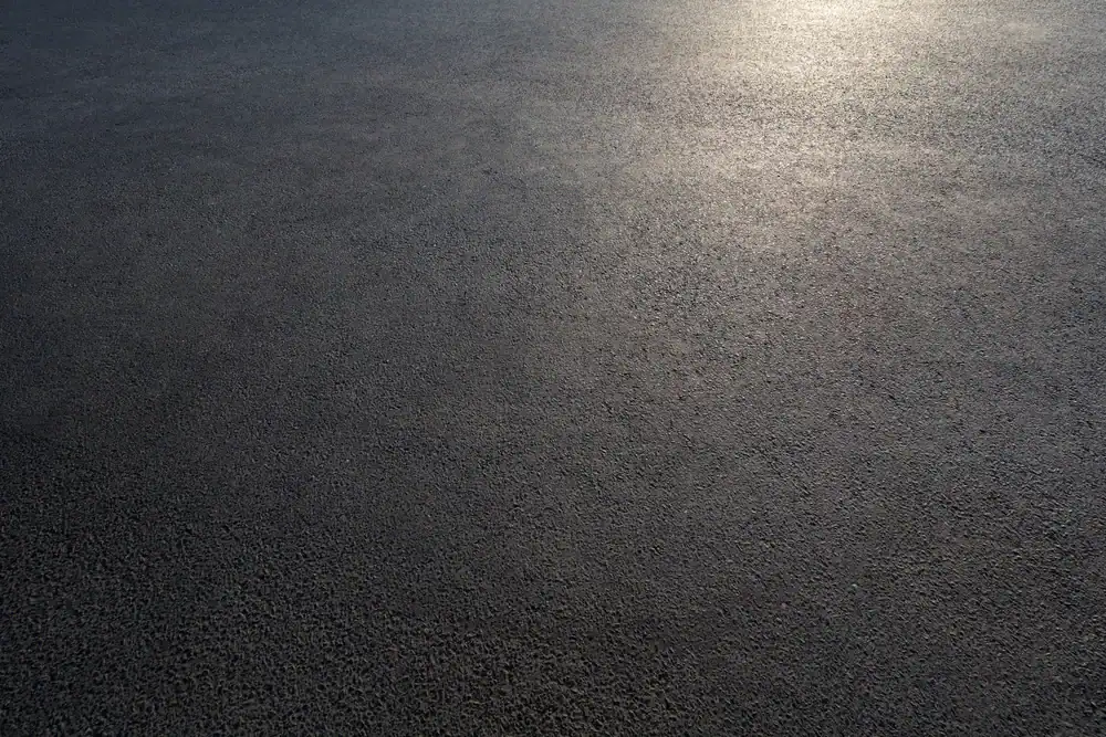 Close-up view of an empty, smooth asphalt surface in Hernando County, FL, with sunlight softly reflecting on the upper right area, creating a gentle gradient across the textured pavement.